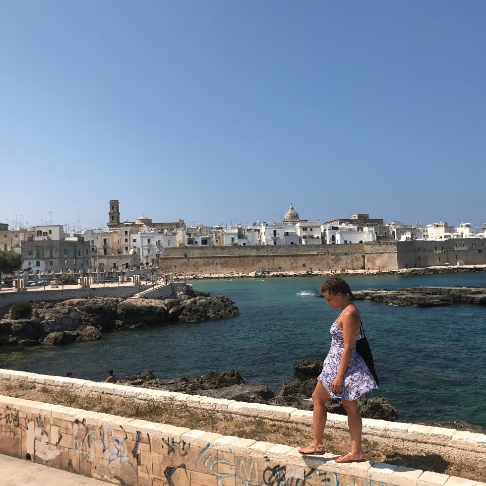 Donna cammina su un muretto e sullo sfondo Monopoli - Bari, Puglia, Italia