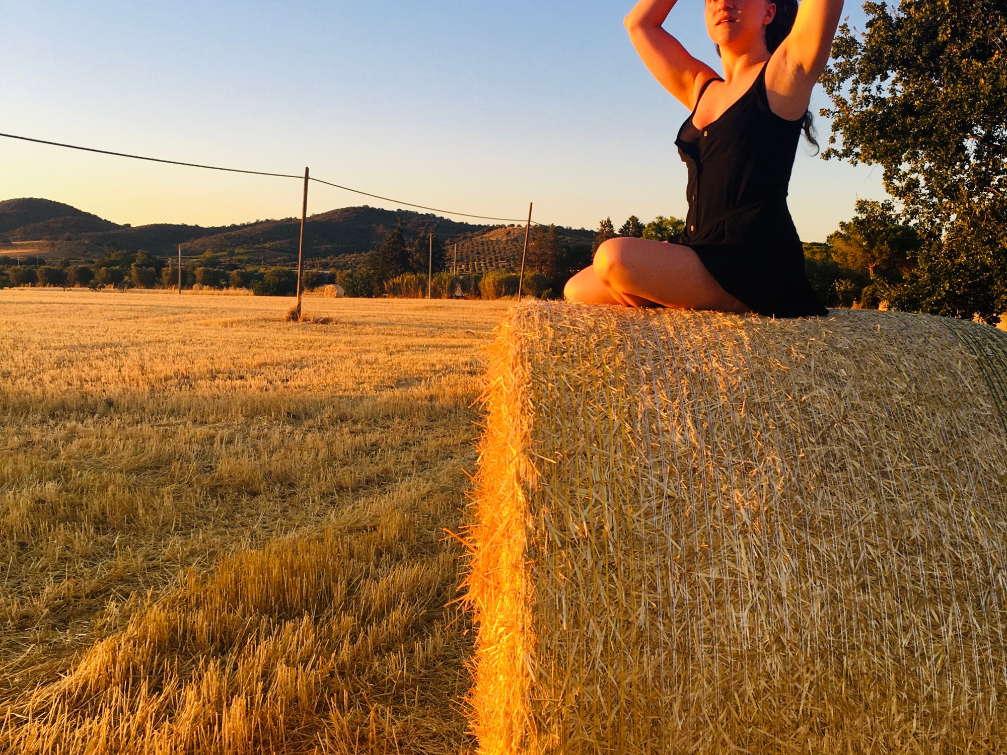 Donna posa su una balla di fieno al tramonto - Maremma toscana, Italia